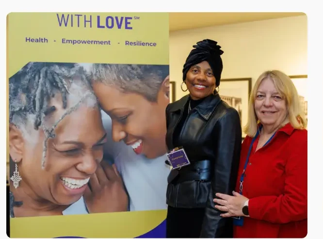 Attendees posing in front of the For HER with LOVE banner
